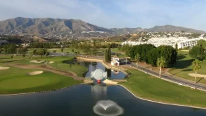 Aerial view the Mijas Los Lagos course with the lake and large metal golf ball in foreground and Sierras de Mijas in the background.