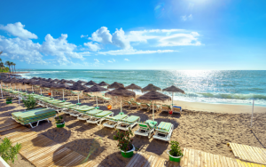 View of the beautiful Benalmadena beach with green sunbeds, parasols, golden sand, Mediterranean ocean and blue sky.