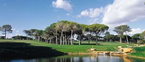 The Vilasol golf course in Portugal with pine trees and fluffy white clouds in the background.