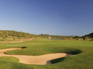 One of the greens at Morgado golf with bunker to the front and clear blue sky.