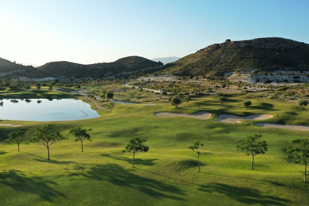 Font del Llop golf course with a lake to the left and surrounded by small mountains in the background.