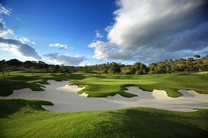 Las Colinas golf course green with large bunkers in the foreground and a cloudy sky.