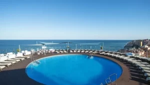 Rooftop circular pool at Hotel El Puerto, offering panoramic views of the Mediterranean Sea, surrounded by sun loungers under a clear blue sky.