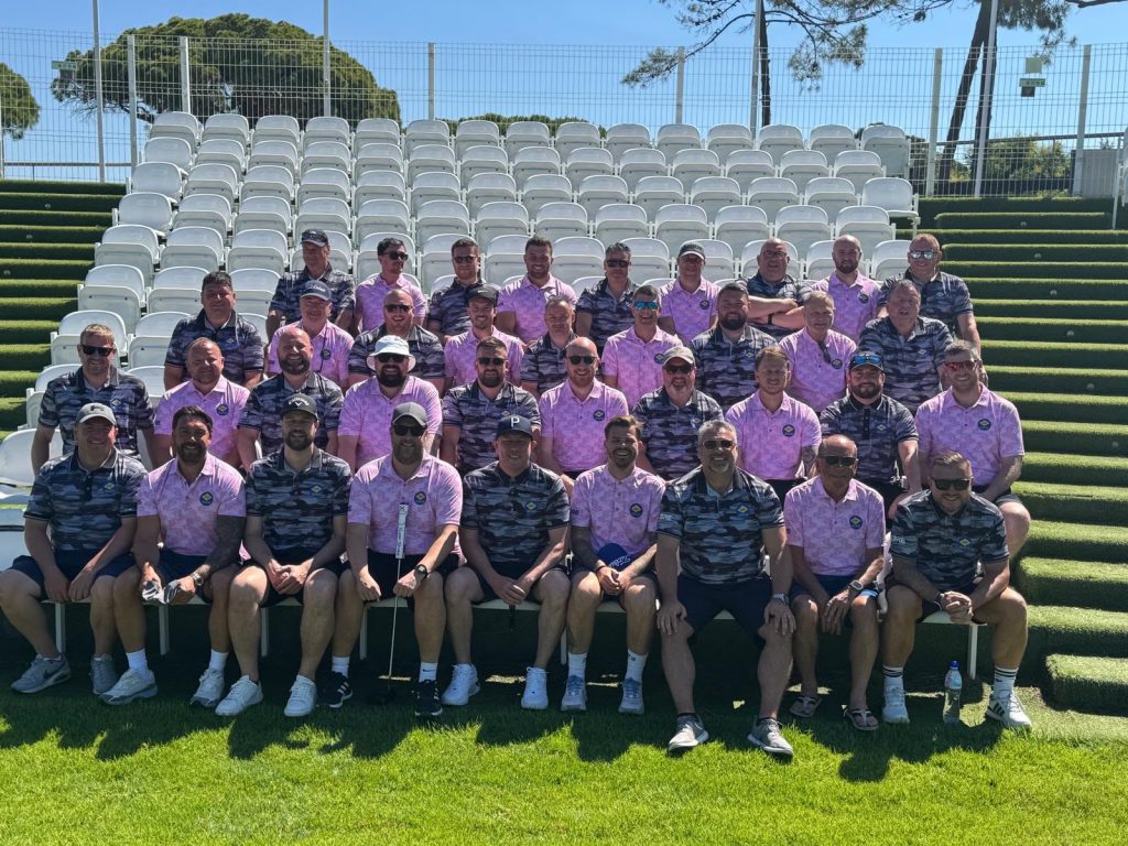 A group of corporate golfers sitting, and posing for a group photo.