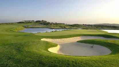 One of the greens at the Royal Obidos course with a lake behind and a bunker in the front with rake.
