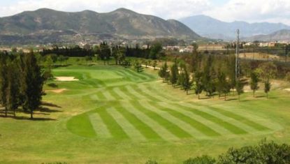 The well-maintained golf course at Guadalhorce, with a green fairway, a sand bunker, and mountains in the background under a cloudy sky.