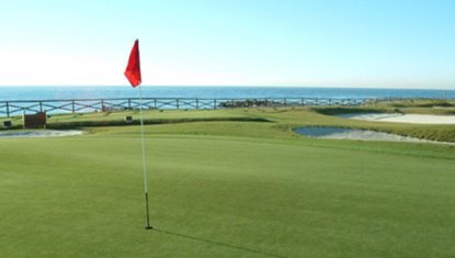 Scenic view of a golf course with a red flag, overlooking the ocean at Guadalmina golf course.