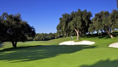 Scenic view of Valderrama golf course featuring lush greens, sand traps, and surrounding trees under a clear blue sky.